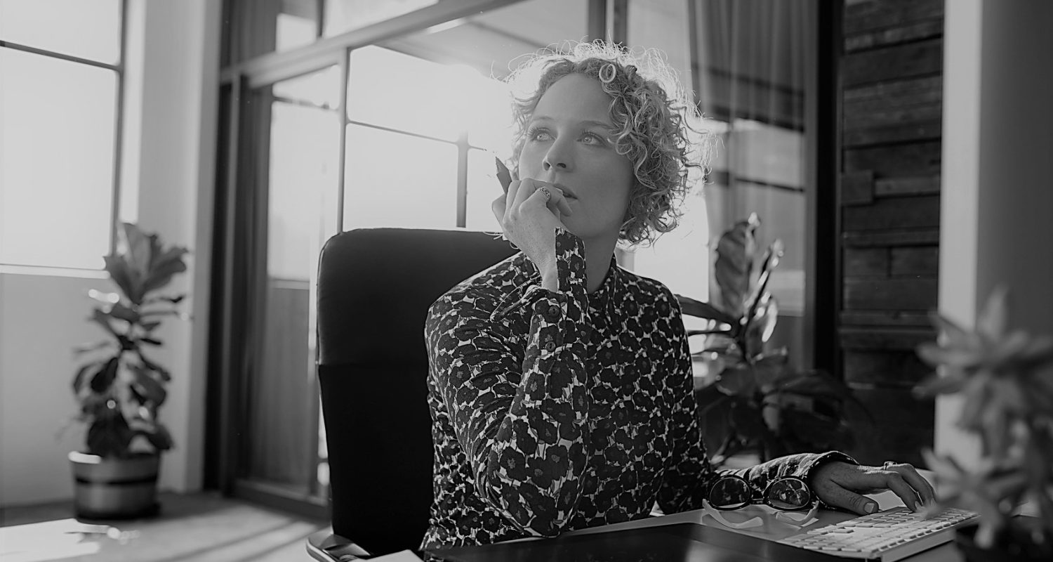 Portrait of young female designer sitting at her desk looking away and thinking.