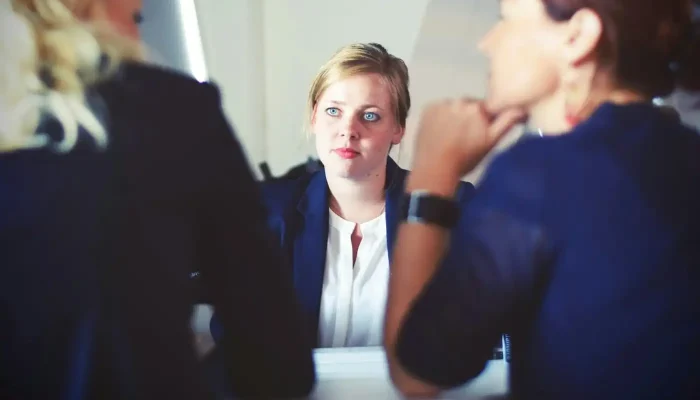 c531b2-20240710-woman-looking-across-a-conference-table-at-two-other-women-in-suits-webp1400