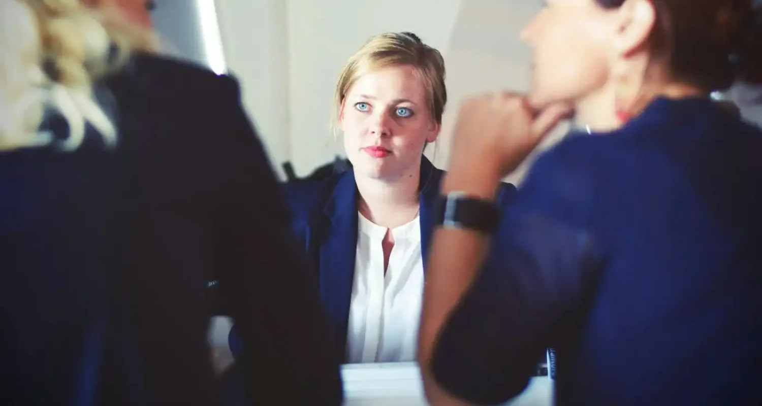 Woman looking across a conference table at two other women in suits.