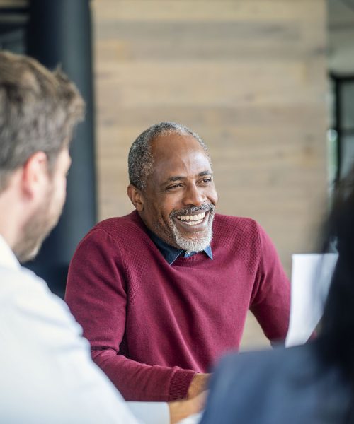 Smiling mature male manager sitting with colleagues in board room. Multi-ethnic professionals are planning strategy during meeting. They are at new office.