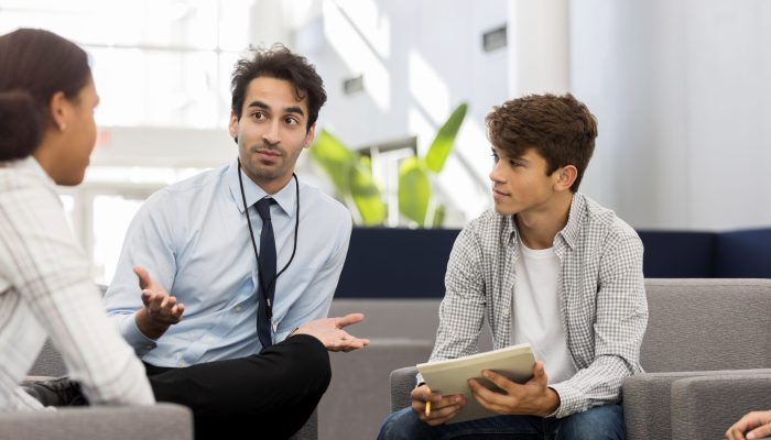 Mid adult male high school counselor gestures while discussing college options with a group of students.