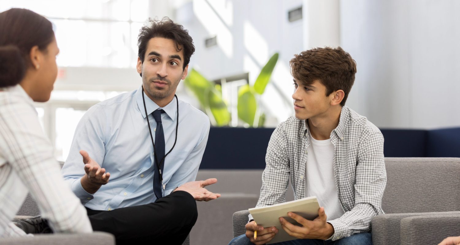 Mid adult male high school counselor gestures while discussing college options with a group of students.