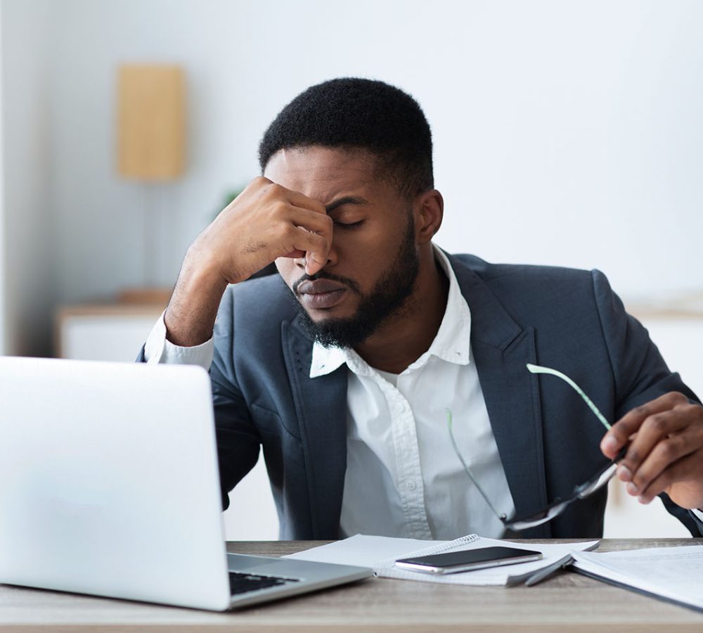 African businessman massaging his nose bridge, tired of long time work on laptop, copy space