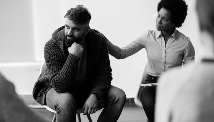 African American psychotherapist encouraging a man who is talking about his problems during group therapy. Focus is on man.