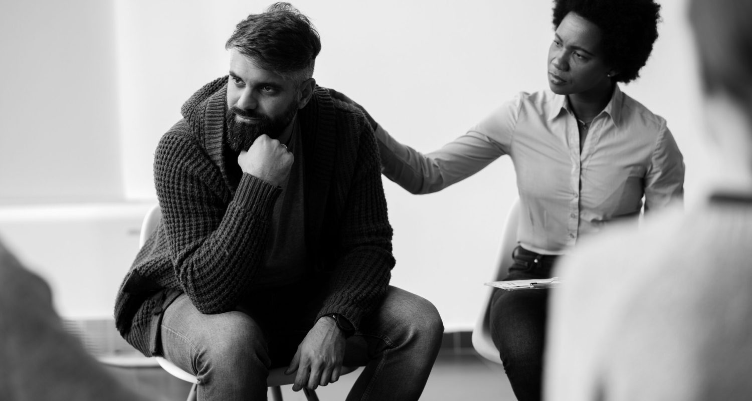 African American psychotherapist encouraging a man who is talking about his problems during group therapy. Focus is on man.