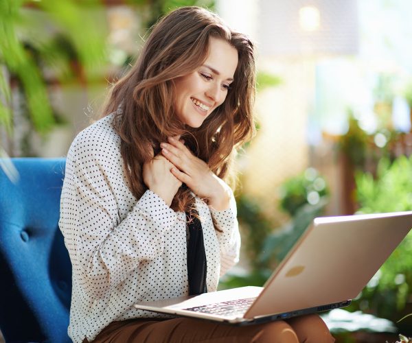 Green Home. happy young woman with long wavy hair in the modern house in sunny day having online meeting on a laptop.