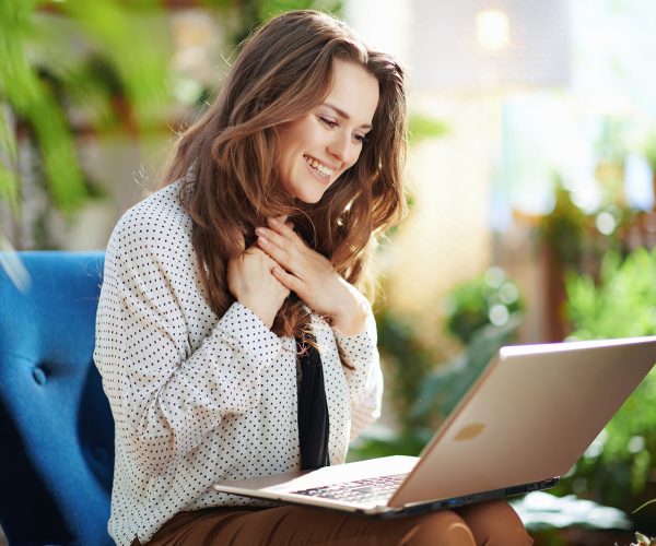 happy woman in sunny day having online meeting Green Home. happy young woman with long wavy hair in the modern house in sunny day having online meeting on a laptop.
