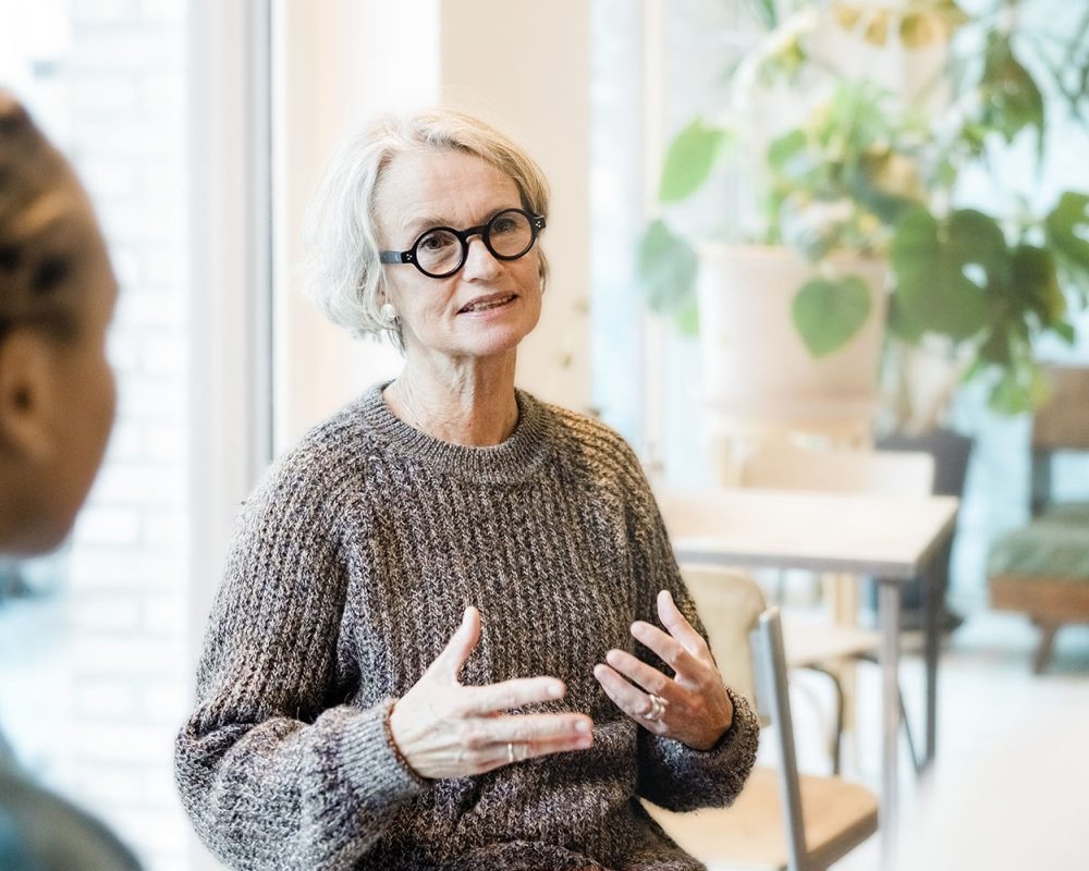 Senior woman talking with participants in a group therapy session. Female sharing her story with support group sitting around.