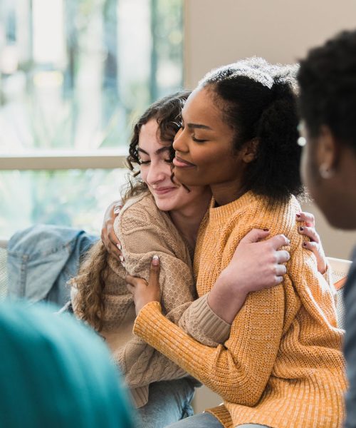 The beautiful friends hug and comfort each other after being vulnerable with their group.