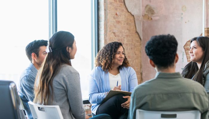 The diverse therapy group listens attentively as the young adult woman shares.