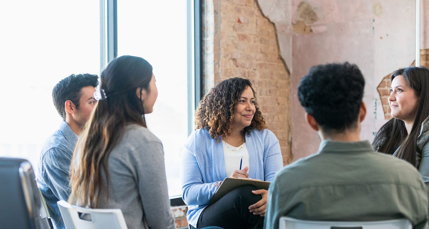 The diverse therapy group listens attentively as the young adult woman shares.