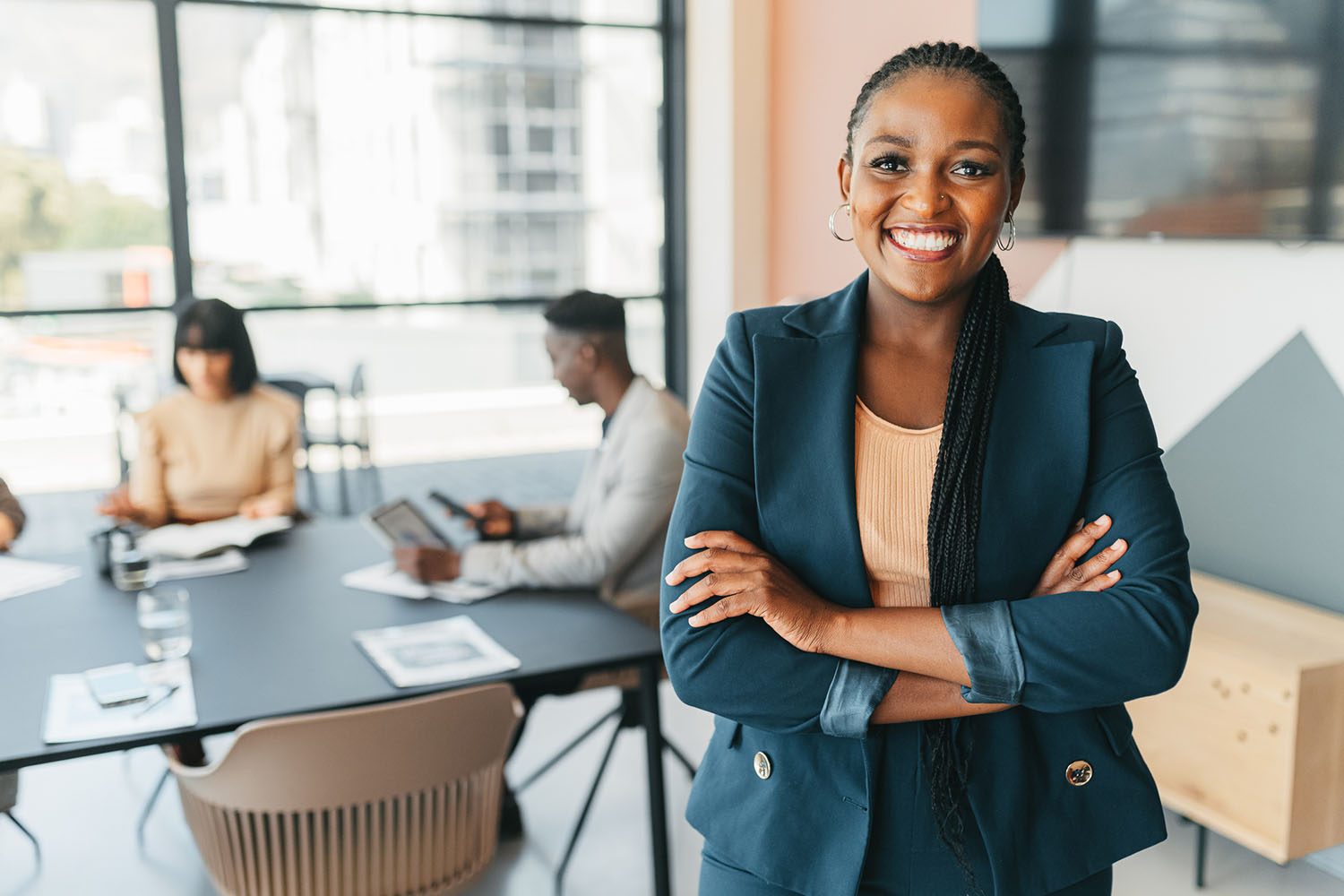 Leader, manager and CEO with a business woman in the office with her team in the background. Portrait of a female boss standing arms crossed at work during a meeting for planning and strategy