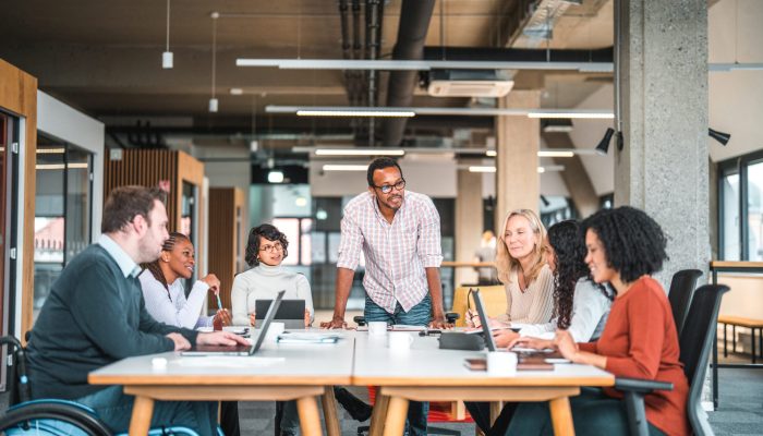 Bright open concept office. There is a work meeting being held where a group of diverse people, including a man on a wheelchair are working together.