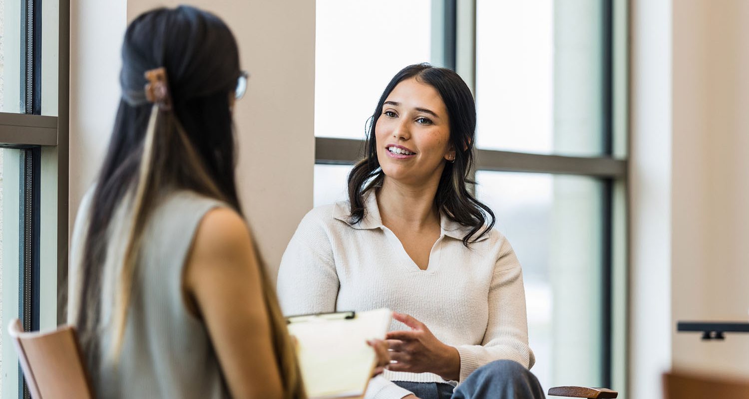 An unrecognizable female manager takes notes during the interview with the young adult woman.