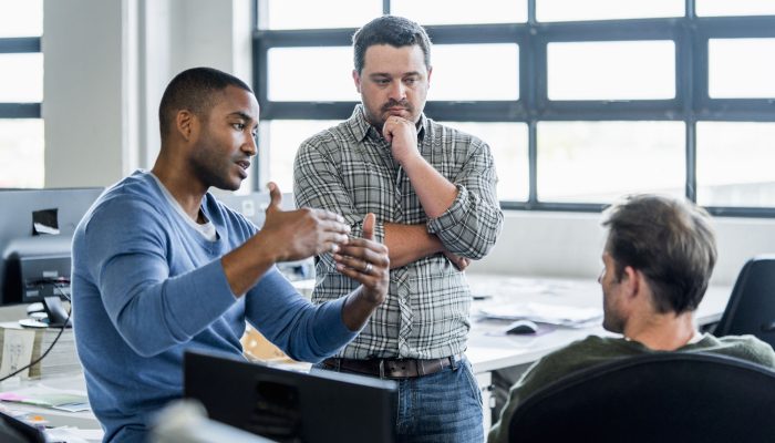 A photo of businessman sharing ideas with colleagues at workplace. Confident male professional is discussing with coworkers. They are wearing smart casuals in creative office.