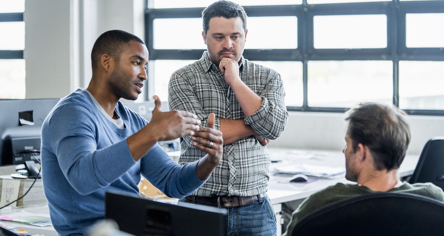 A photo of businessman sharing ideas with colleagues at workplace. Confident male professional is discussing with coworkers. They are wearing smart casuals in creative office.