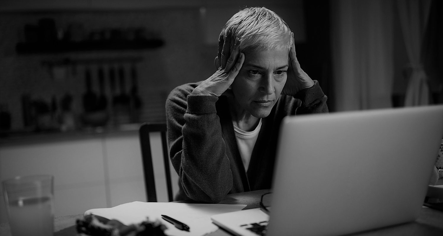 Senior woman working from home late at night. She is holding her head during stressful moments.