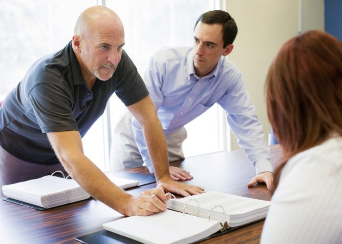 Office worker confidently makes a point during a meeting while his colleague watches him wearily.